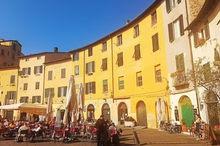 Cafés and colorful historic buildings in Piazza dell’Anfiteatro, Lucca, on a Pisa & Lucca private tour from La Spezia port