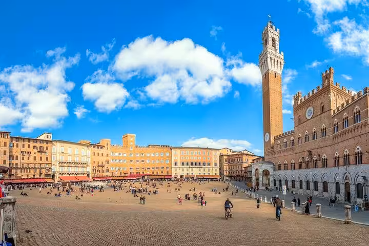 Vibrant Piazza del Campo in Siena with Torre del Mangia under a blue sky, part of a full-day Tuscany tour.
