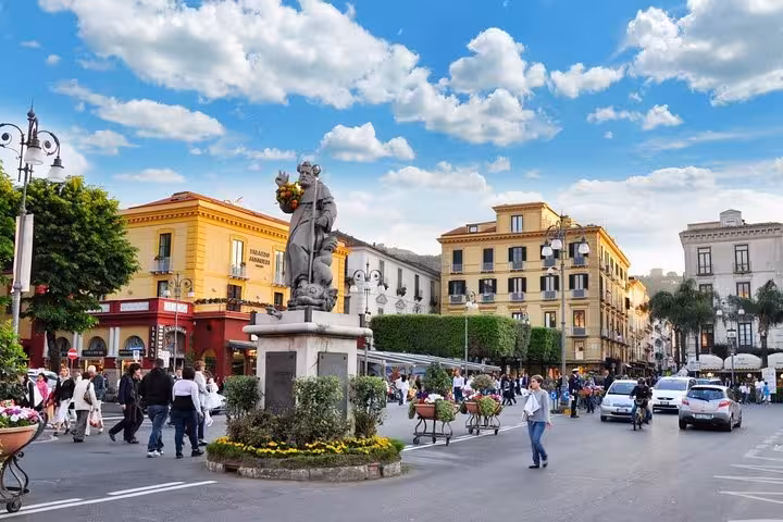Vibrant Piazza Tasso in Sorrento bustling with people and adorned with a historic statue under a bright blue sky.
