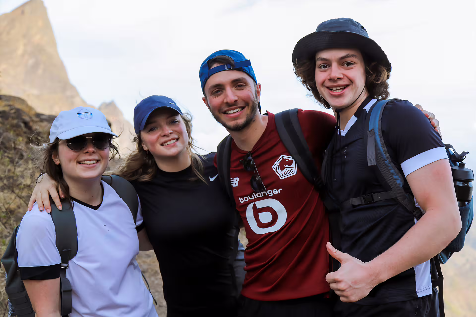 Happy group of friends reach Pico D'Antónia summit during Monte Tchota Natural Park hike, enjoying stunning views.