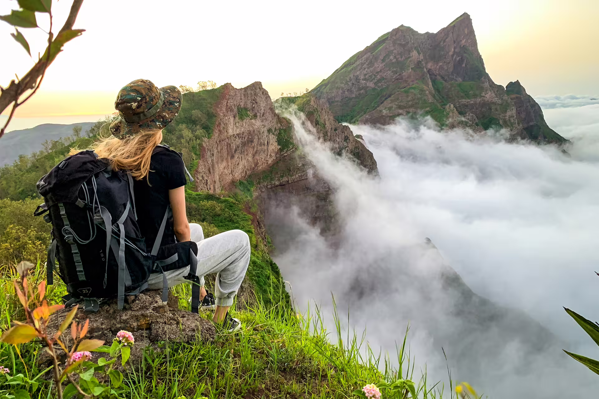 A hiker enjoys breathtaking views of Pico D'Antónia shrouded in clouds from Monte Tchota's summit trail.