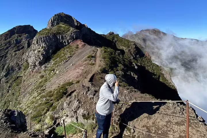 Hiker in a hoodie stands at a viewpoint on Pico do Arieiro, capturing the breathtaking mountain landscape.