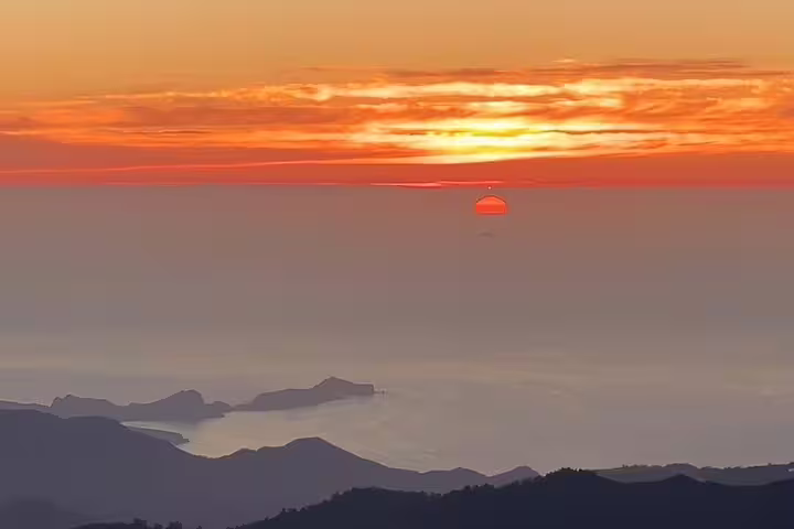 Golden sunrise over Madeira's rugged coastline seen from Pico do Arieiro, offering a tranquil hiking experience.