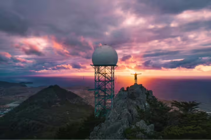 Hiker enjoying sunset views from Pico do Facho Panoramic Trail with a radar tower and ocean in the background.