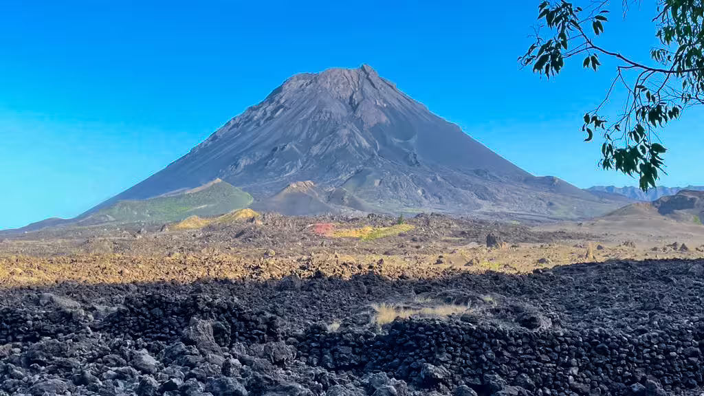 Majestic Pico do Fogo volcano under a clear blue sky, surrounded by rugged volcanic landscape.