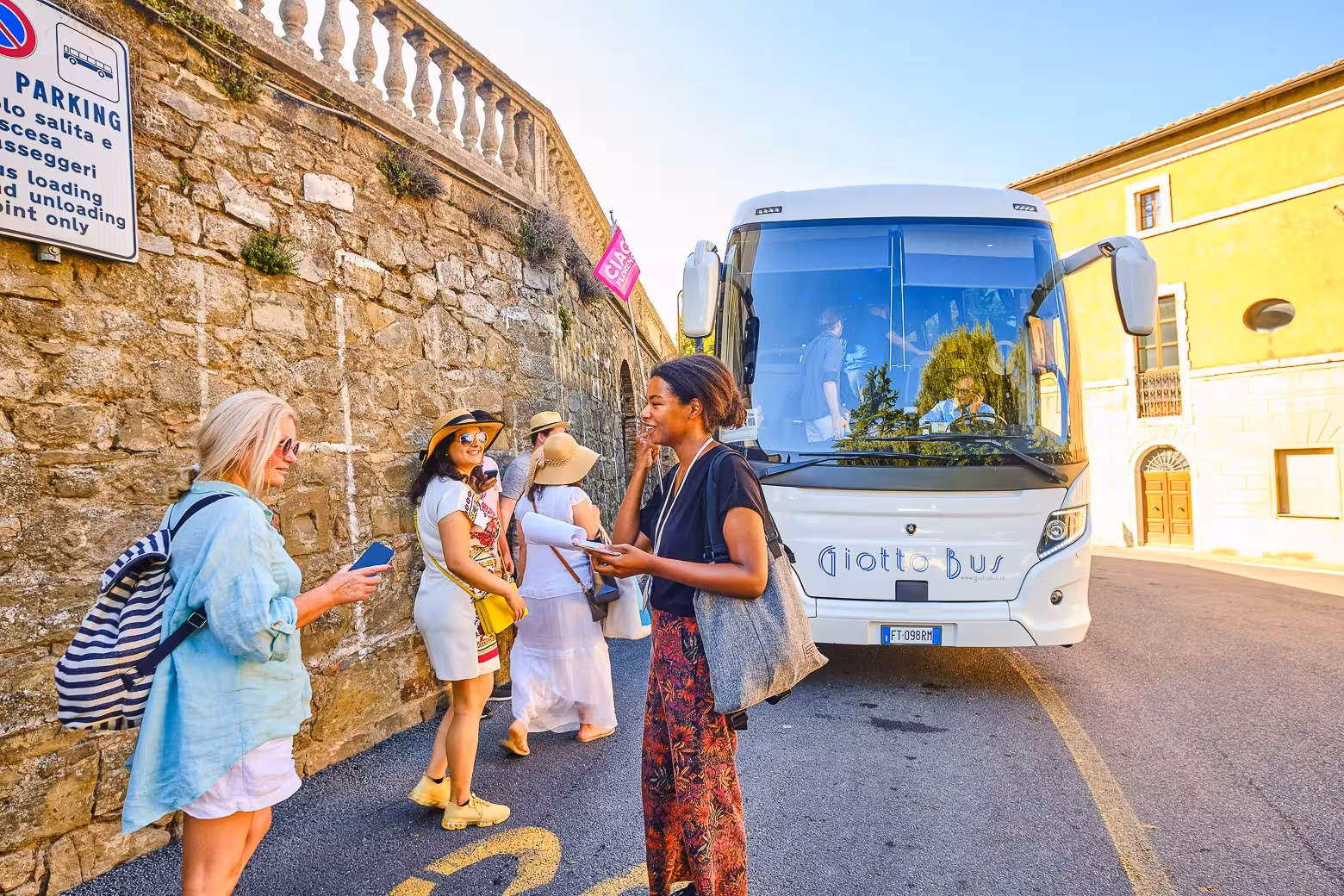 Tourists gather near a Giotto Bus in Pienza, ready to embark on the Land of Brunello wine tasting experience.