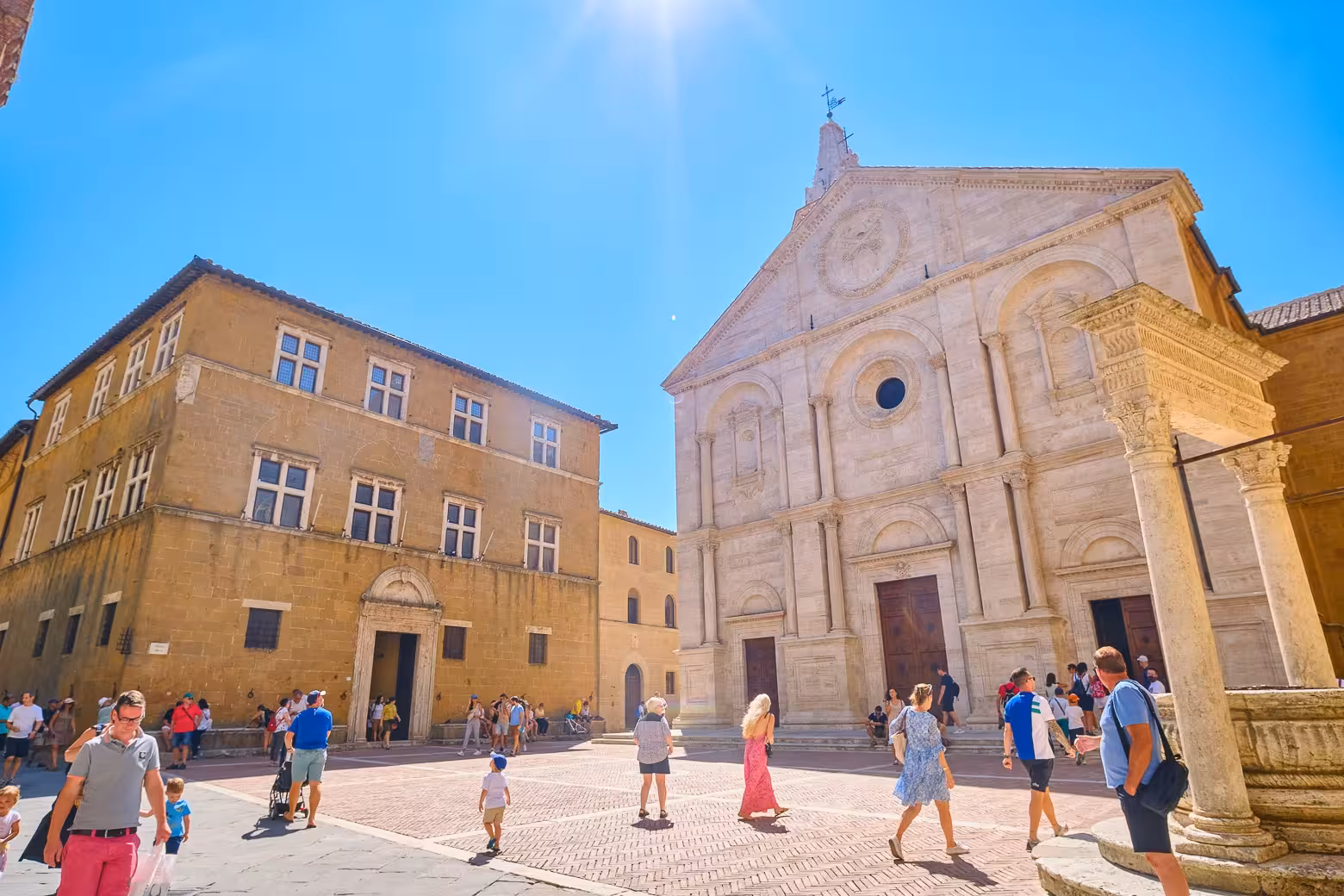 Tourists explore the historic square of Pienza under a bright blue sky during a Val d'Orcia tour from Florence.