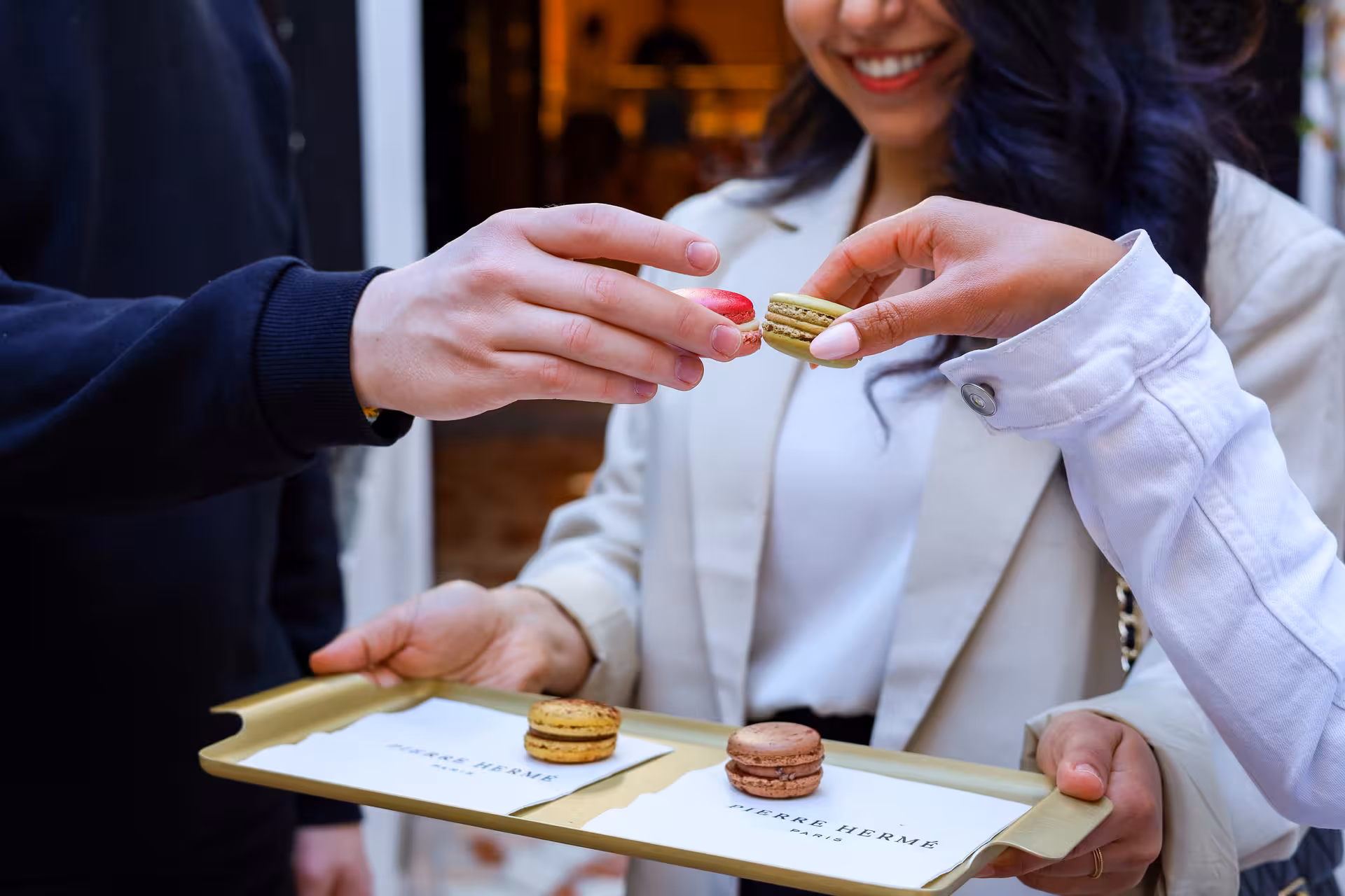 Woman smiling while sampling Pierre Hermé macarons on a gold tray during a Paris food tour