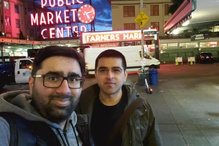 Two men taking a selfie at night in front of Pike Place Public Market Center in Seattle