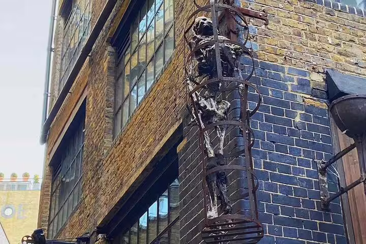 Metal sculpture of a figure climbing a spiral cage on a brick building in Southwark London