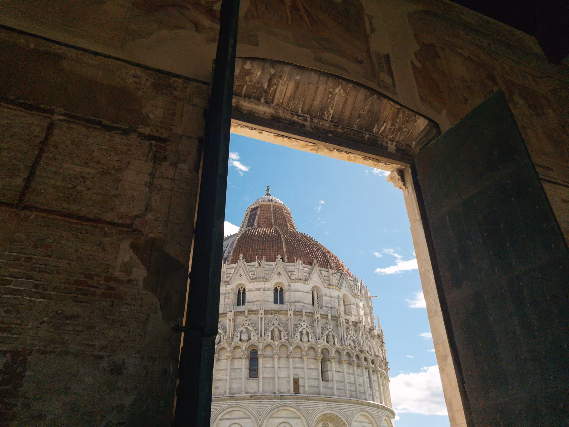 View of Pisa's iconic Baptistery dome through rustic doorway, highlighting architectural beauty on Florence day trip.