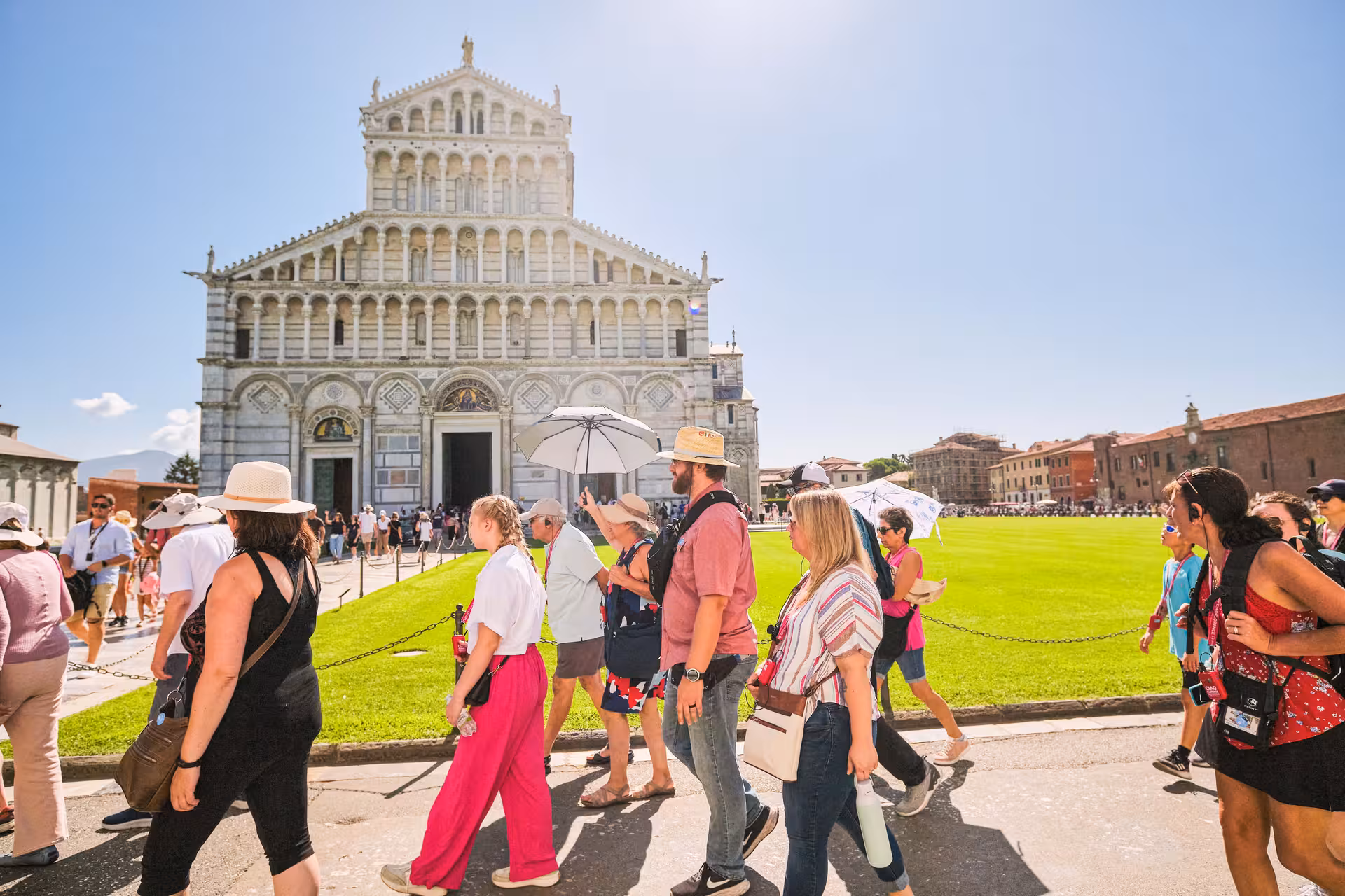 A group of tourists explores the vibrant Piazza dei Miracoli with Pisa Cathedral in the background.