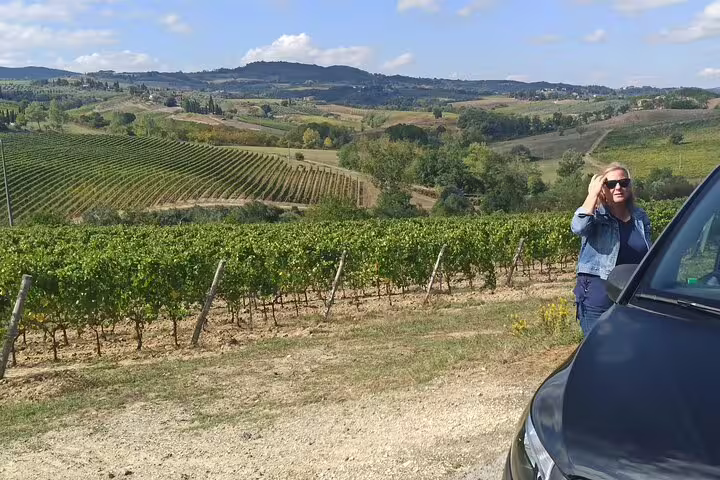 Traveler standing beside car overlooking scenic Chianti vineyards and rolling Tuscan hills on a private Pisa wine tour