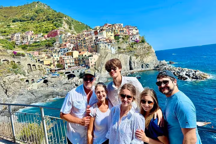 Group of friends smiling in front of Manarola's colorful cliffside buildings and azure sea in Cinque Terre.
