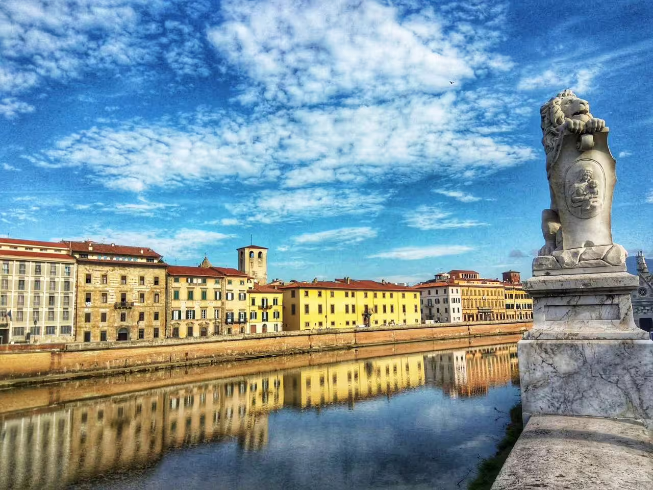 Scenic view of Pisa's historic riverside with vibrant buildings and a lion statue, perfect for eco-friendly tours.