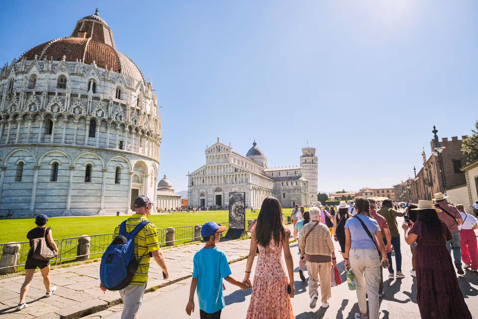 Tourists exploring Pisa's iconic Baptistery and Leaning Tower on a sunny day, part of a Livorno half-day excursion.
