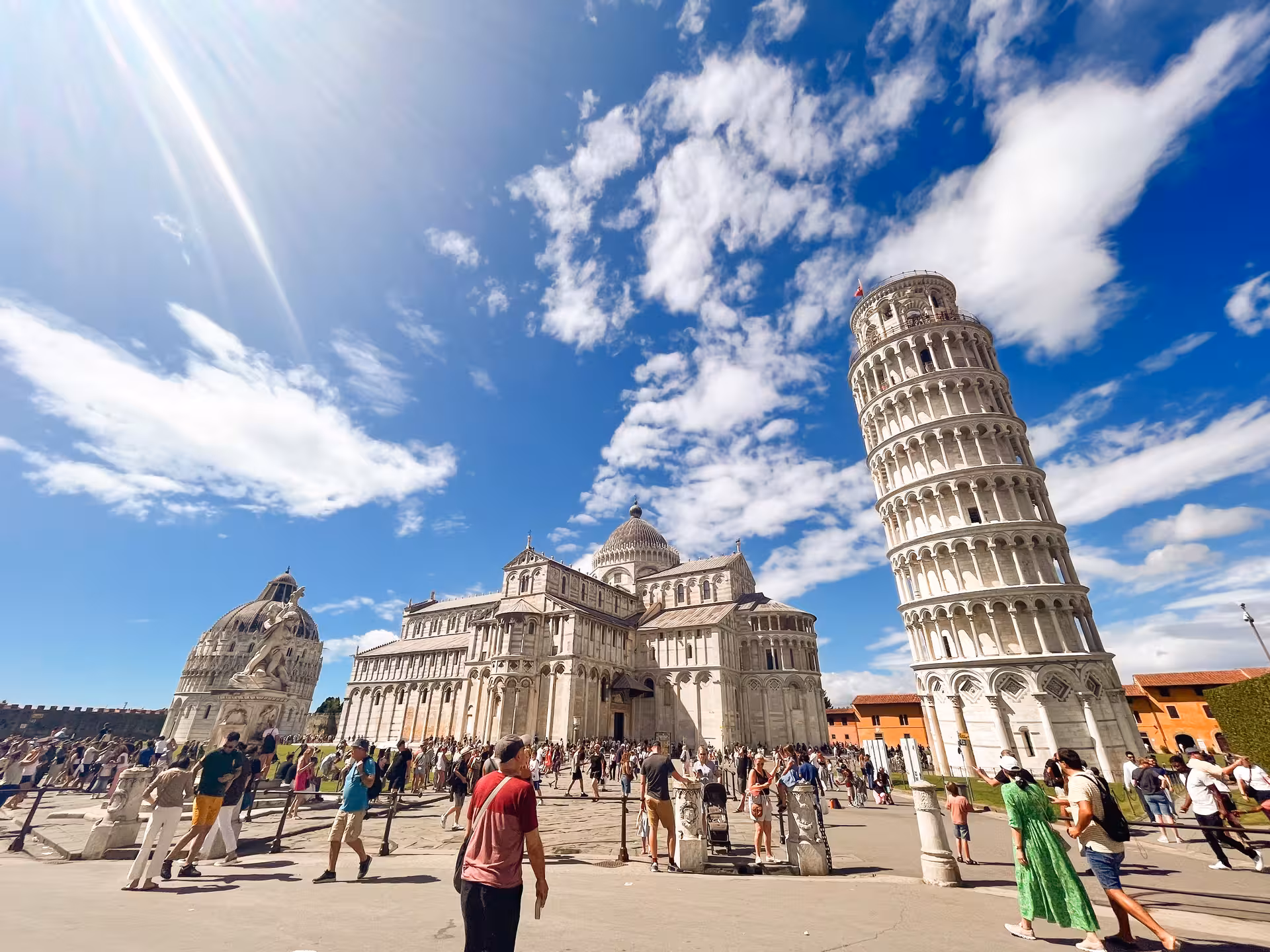 Tourists exploring Pisa's Leaning Tower and Cathedral under a bright blue sky on a private tour from Florence.