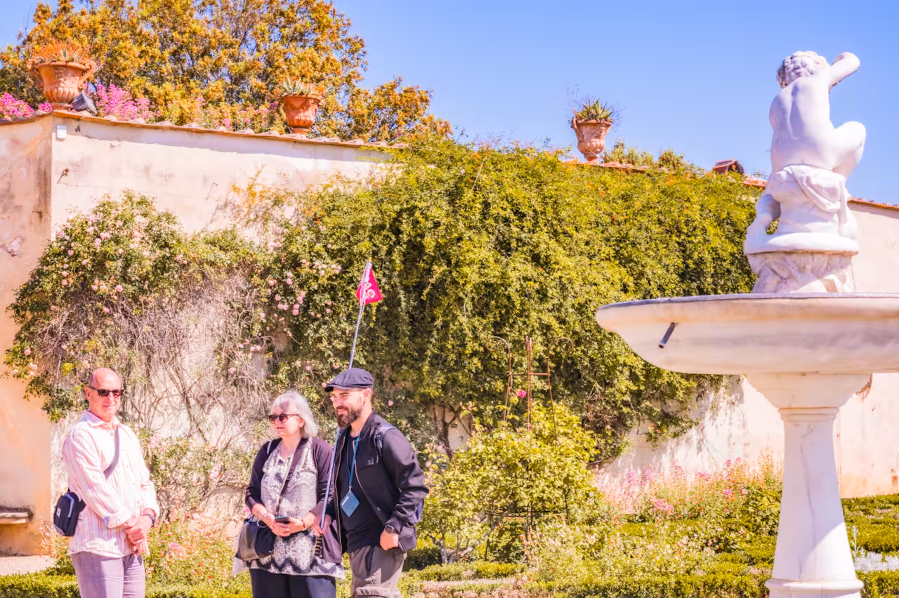 Tour group exploring Boboli Gardens with a guide near a decorative fountain, surrounded by lush greenery.
