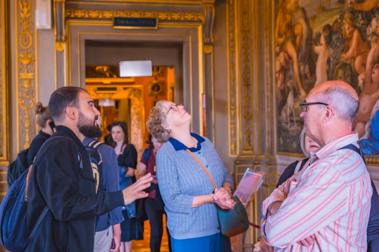 Visitors engaged in a guided tour inside the ornate halls of Florence's Pitti Palace.