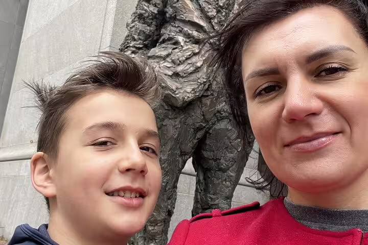 Woman and boy smiling in selfie beside bronze statue during Pittsburgh landmarks tour