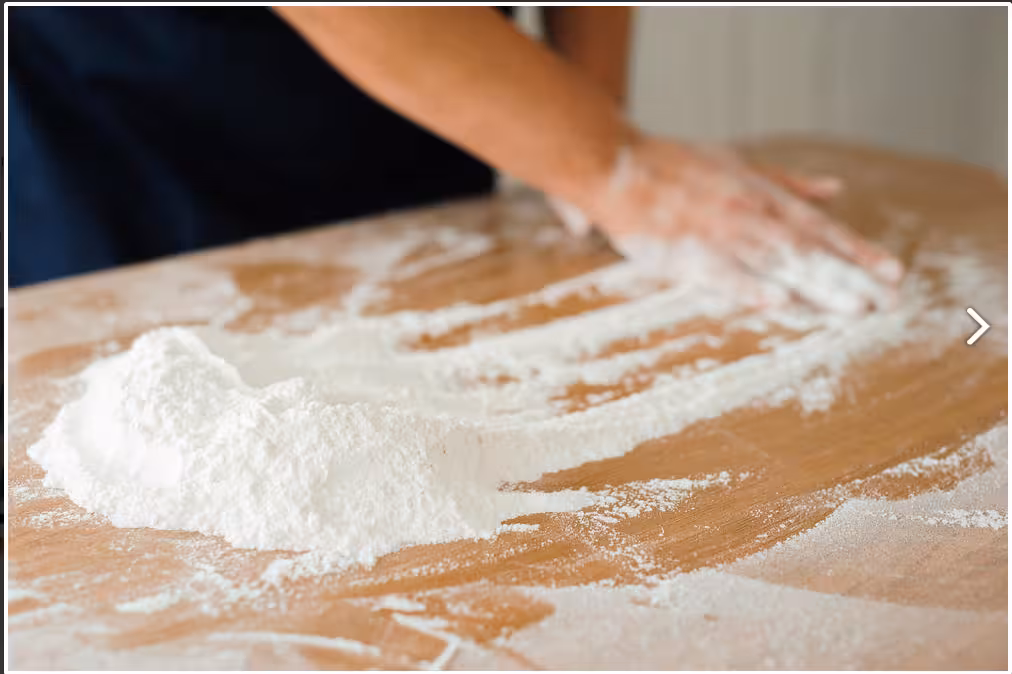 Hands expertly spread flour on a wooden table during a pizza-making class in Naples.