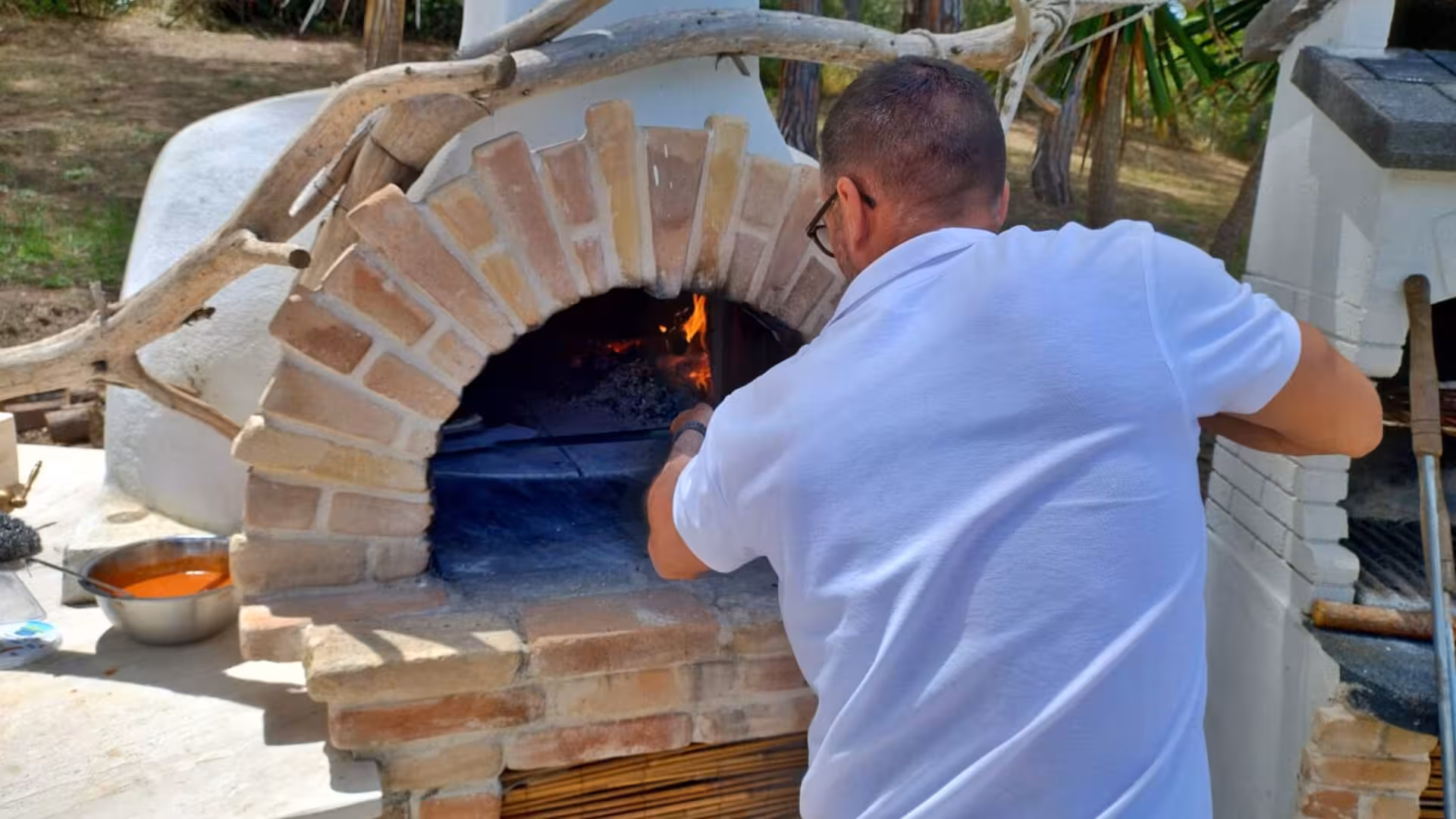 Instructor tending a wood-fired oven, igniting flames for an authentic pizza-making experience in a villa setting.