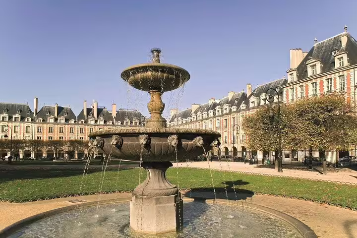 Ornate stone fountain in Place des Vosges square, Le Marais, Paris, with historic red-brick buildings
