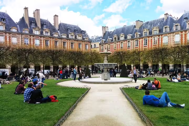 Visitors relaxing on grass at Place des Vosges fountain courtyard in Le Marais, Paris