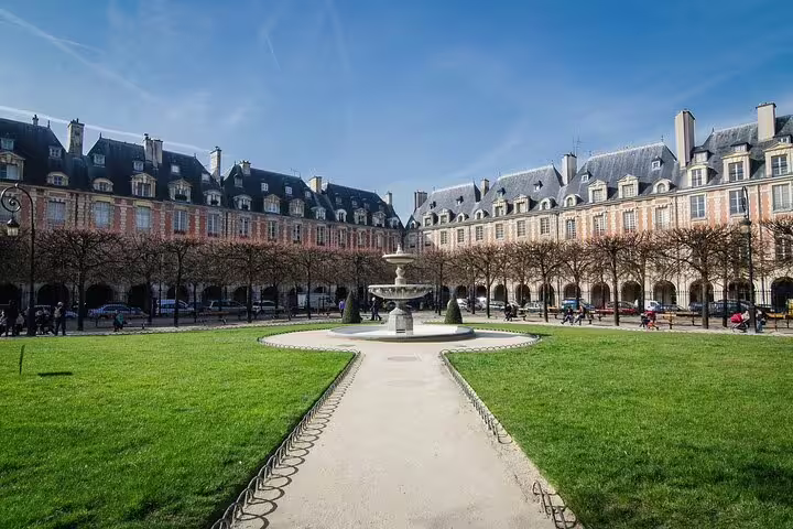 Place des Vosges square in Le Marais Paris with fountain, green lawns, and historic red brick buildings