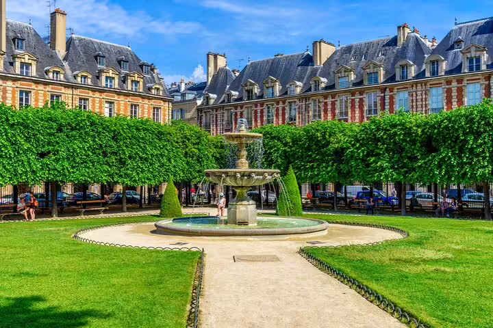 Place des Vosges fountain and manicured gardens in Le Marais, Paris, surrounded by historic red brick arcaded buildings