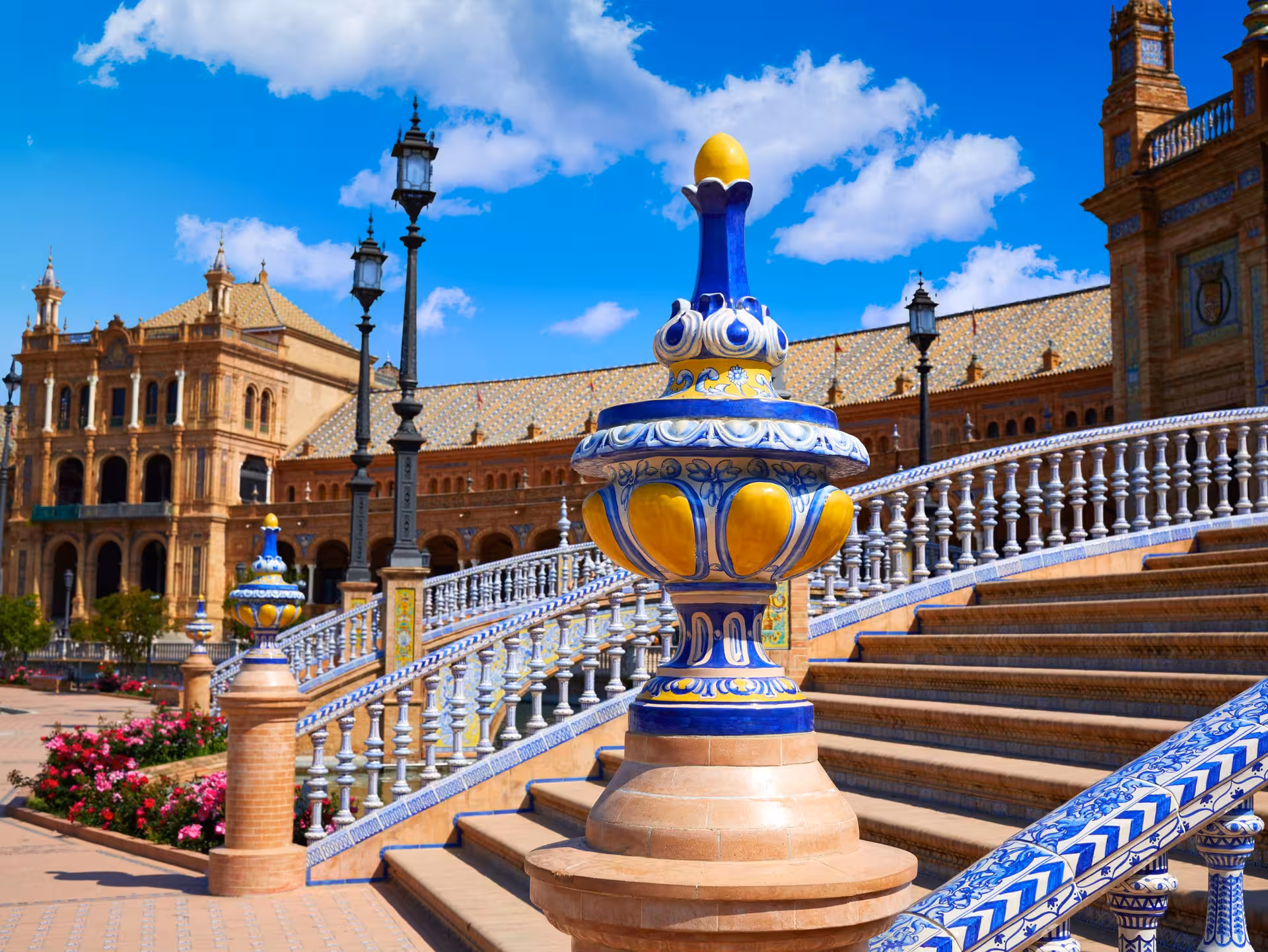 Vibrant ceramic balustrades and grand architecture at Plaza de España in Seville, Spain, under a bright blue sky.