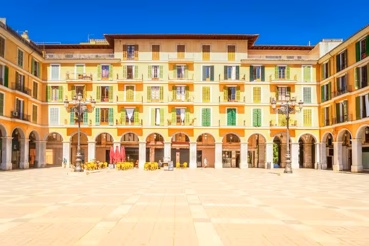 Colorful arcaded buildings surrounding Plaza Mayor in Palma de Mallorca on a sunny day