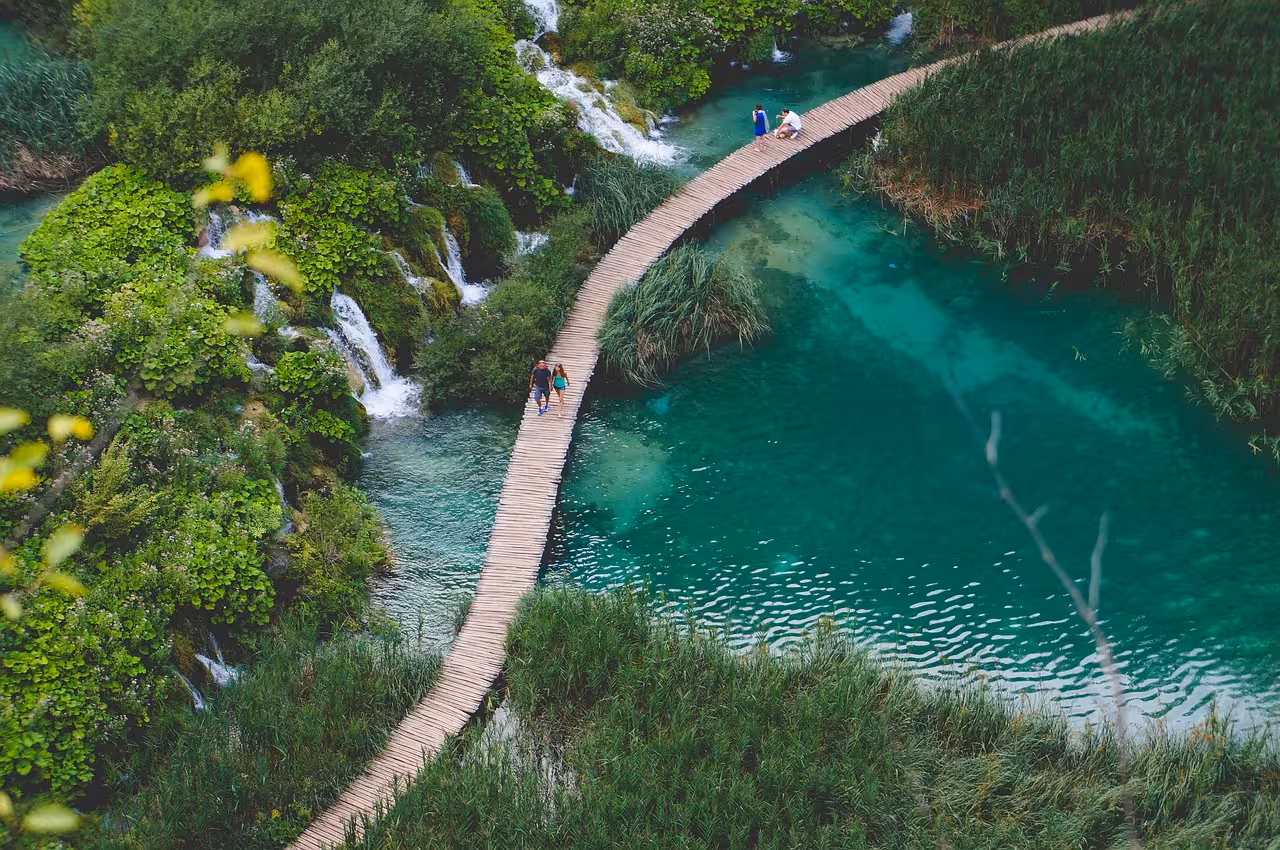 Wooden boardwalk over turquoise water and waterfalls in Plitvice Lakes National Park tour from Split