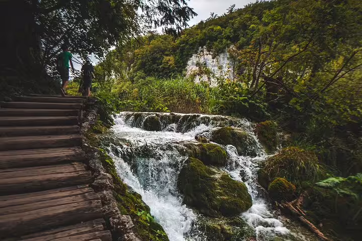 Wooden boardwalk beside cascading waterfalls on a Plitvice Lakes economy scheduled tour in Croatia