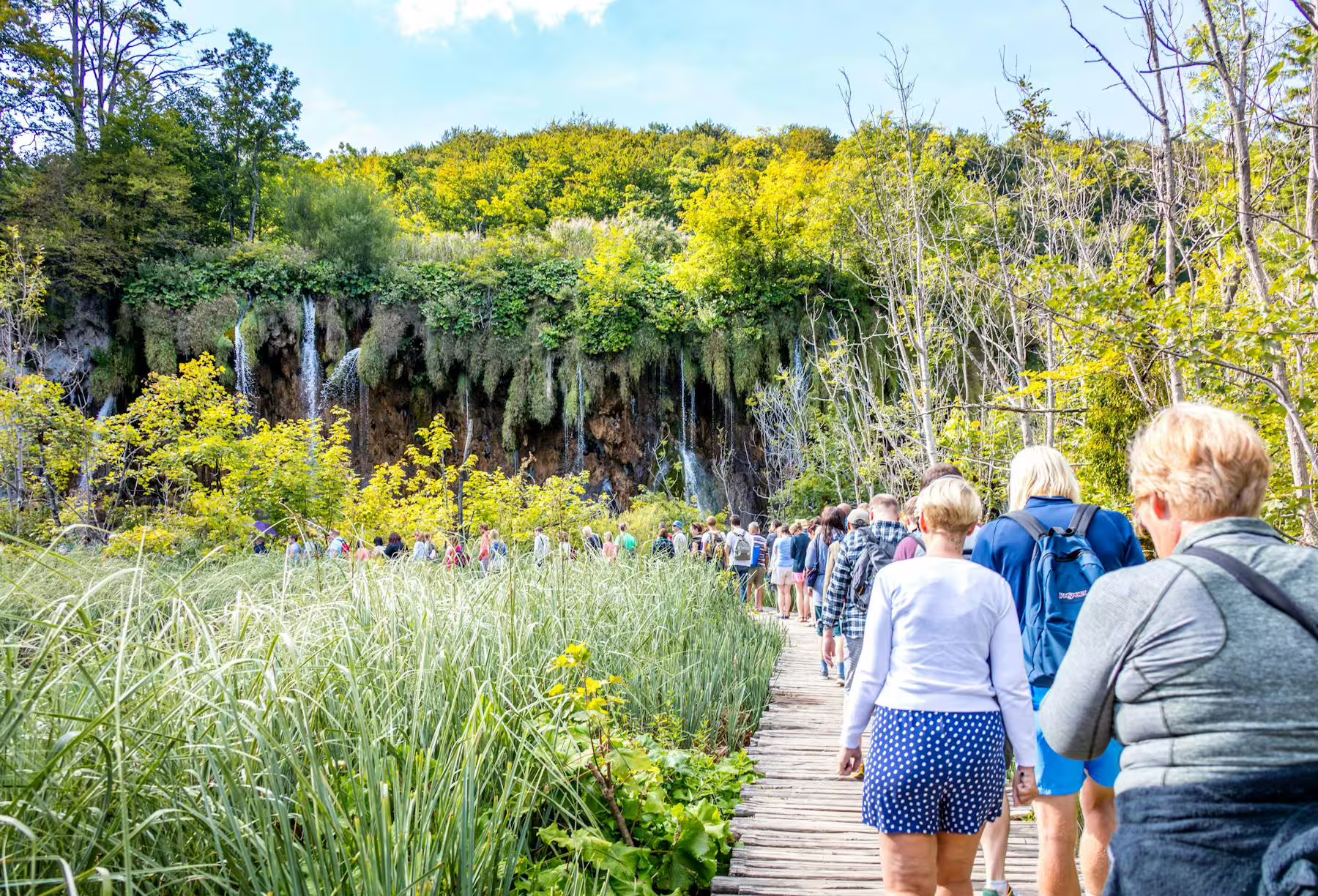 Guided Plitvice Lakes day trip from Zadar and Biograd, hikers on boardwalk toward waterfalls in Croatia
