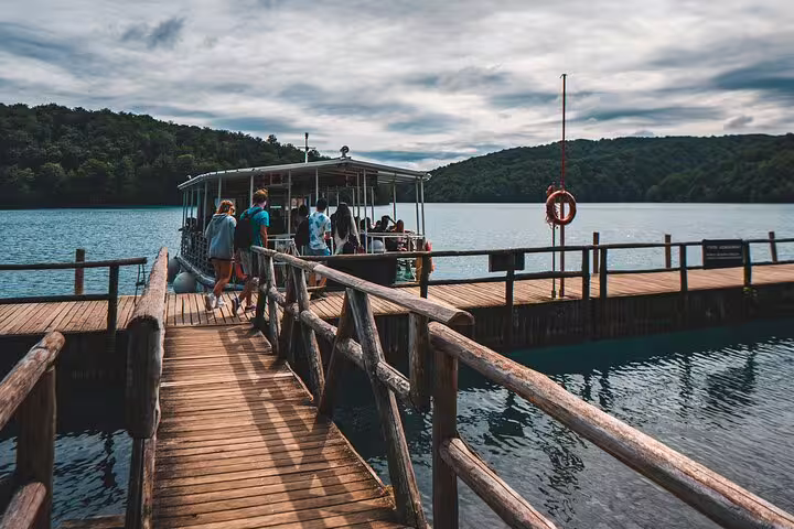 Visitors boarding electric boat from wooden pier on Plitvice Lakes scheduled guided tour in Croatia