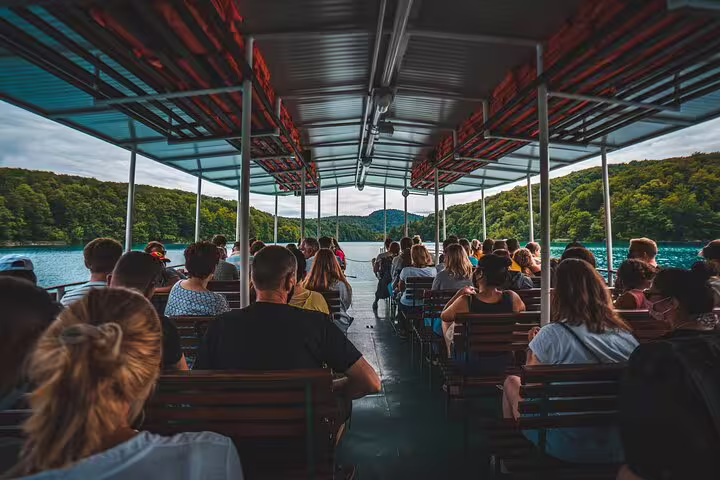 Boat ride with tour group on Plitvice Lakes guided tour, cruising turquoise lake between forested hills