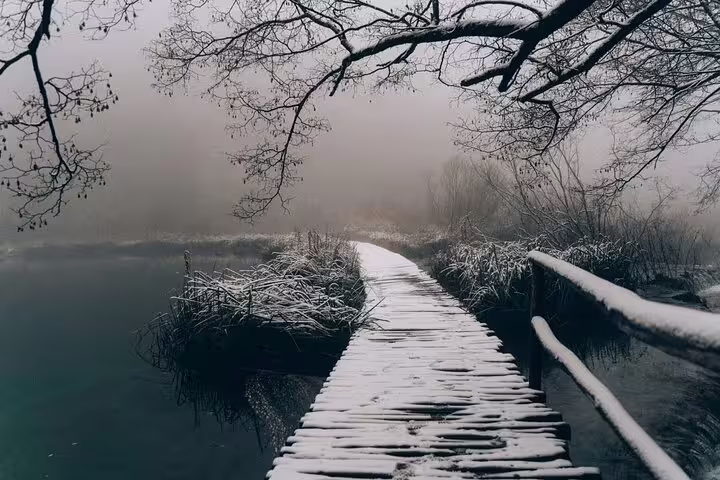 Snowy wooden boardwalk over misty Plitvice Lakes, Croatia, winter tour with secured tickets and boat ride