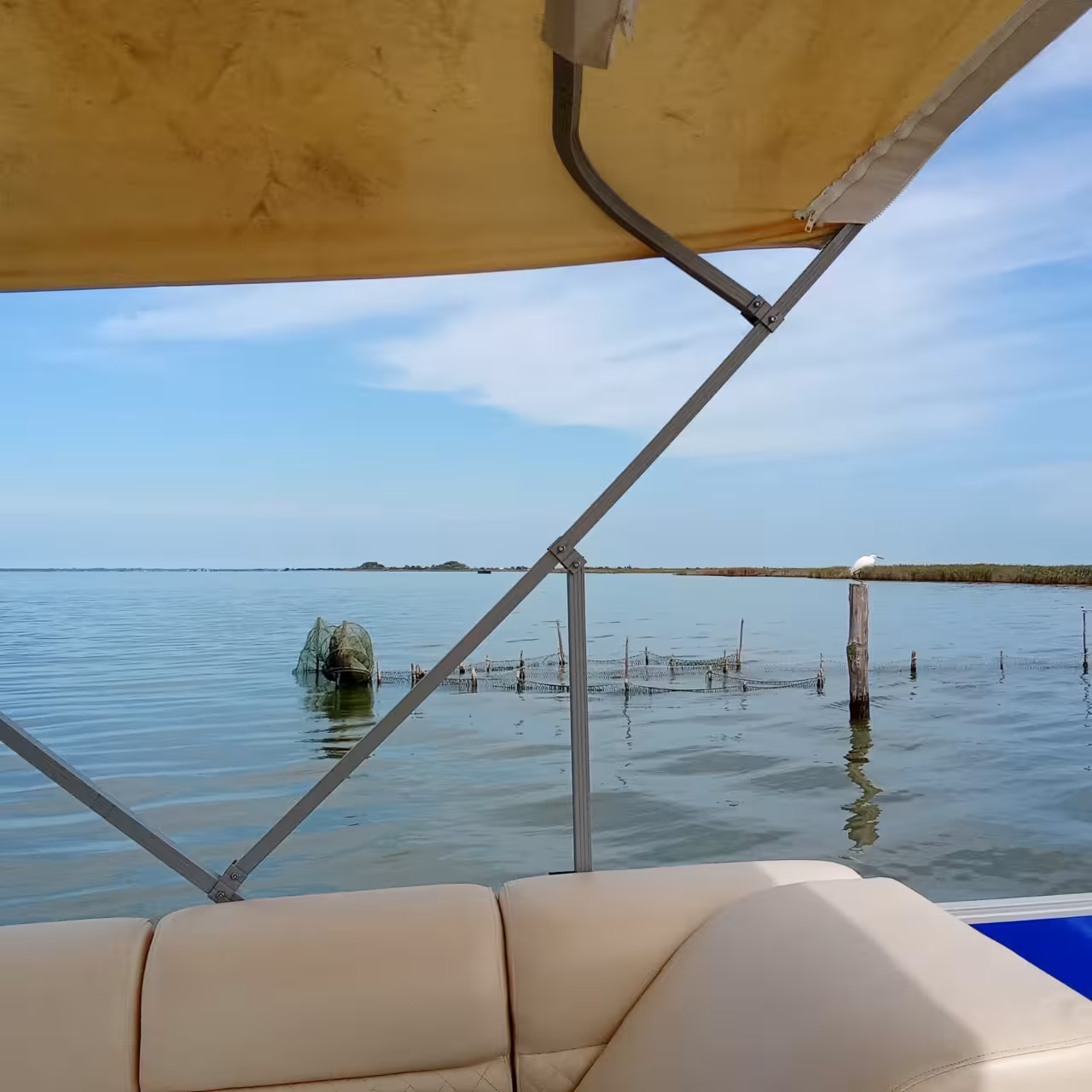 View from boat canopy across calm Po Delta waters and fishing nets, Isola dell’Amore nature cruise
