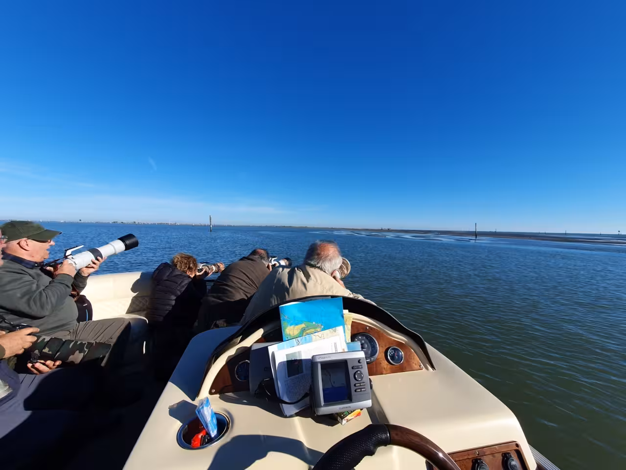 Wildlife photographers on a Po Delta boat tour scanning the lagoon near Isola dell’Amore under clear blue skies