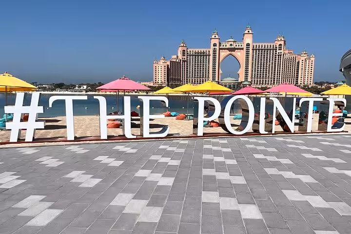 The Pointe Palm Jumeirah waterfront sign with Atlantis hotel view, photo stop on Dubai private city tour
