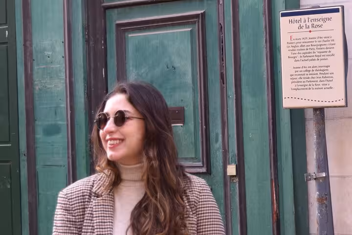 Smiling woman stands beside historic green door with Hôtel à l'enseigne de la Rose sign during Poitiers walking tour.