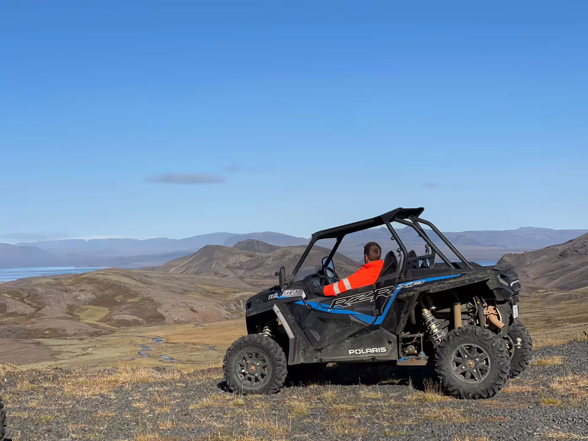 Person in orange jacket sitting in a Polaris RZR buggy overlooking Iceland highland valleys and a fjord