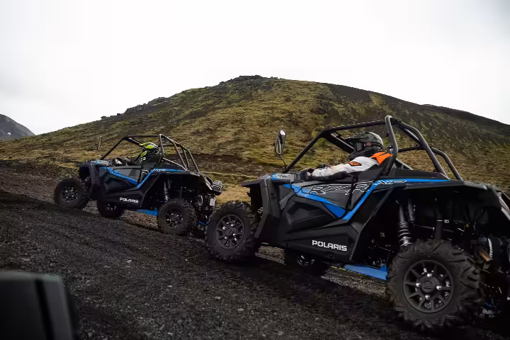 Two Polaris RZR buggies on volcanic terrain with green hillside in Iceland