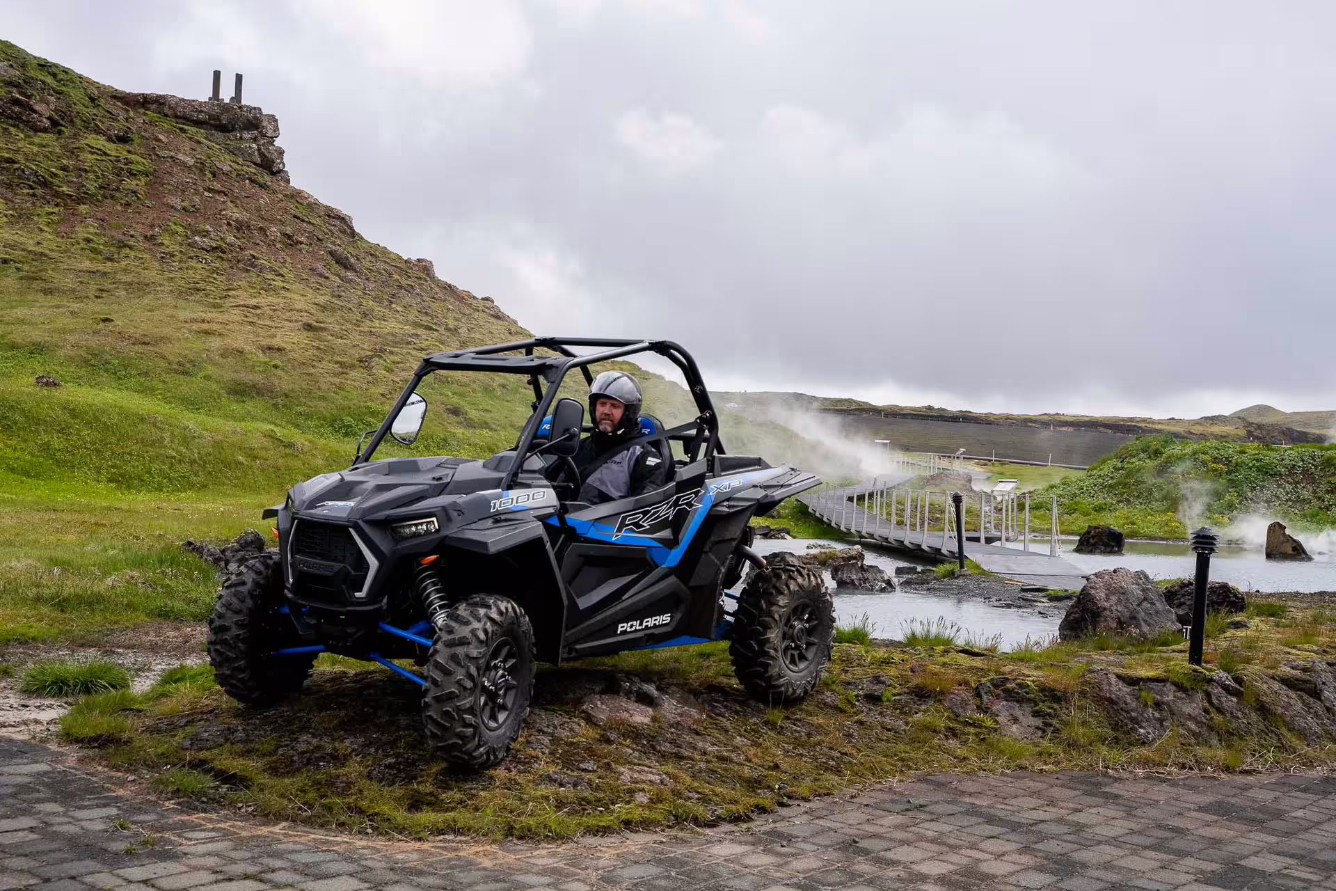 Man driving Polaris RZR buggy near geothermal hot spring pool in Iceland