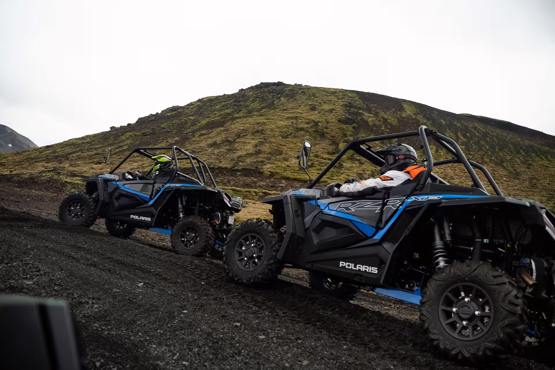 Two Polaris RZR XP buggies on volcanic gravel terrain with green mossy hills in Iceland