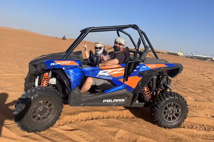 Couple riding Polaris RZR dune buggy quad bike on desert safari, off-road adventure on golden sand dunes