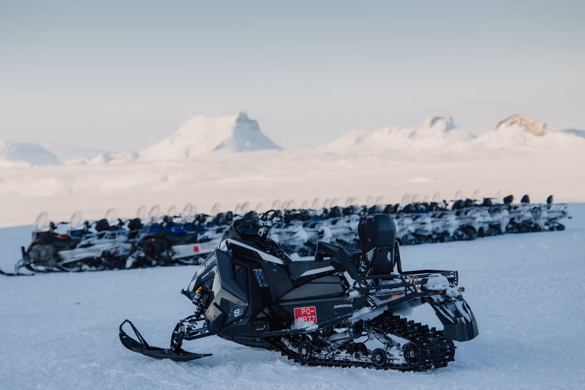 Polaris snowmobiles parked on an Icelandic glacier with snow-capped mountains in the background during a Golden Circle snowmobile tour from Reykjavik.