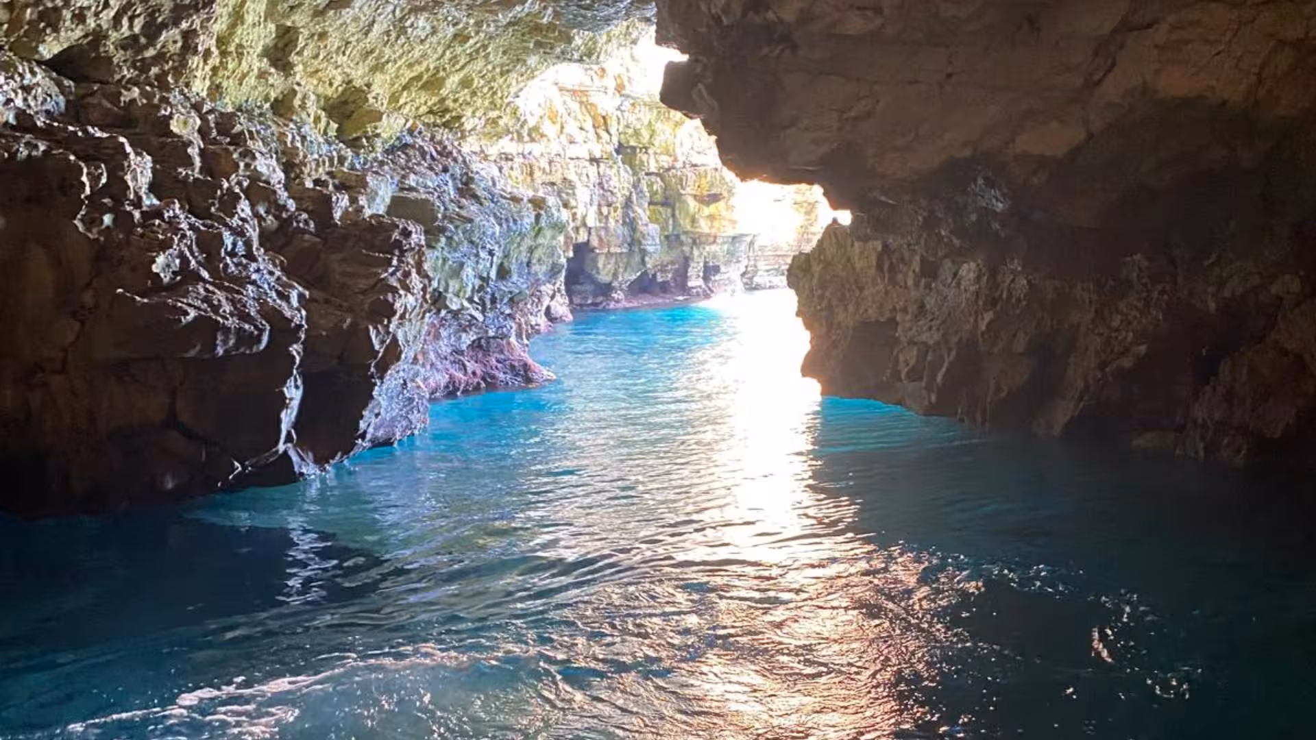 Sunlit entrance of a sea cave in Polignano a Mare, showcasing turquoise waters and rugged rock formations.