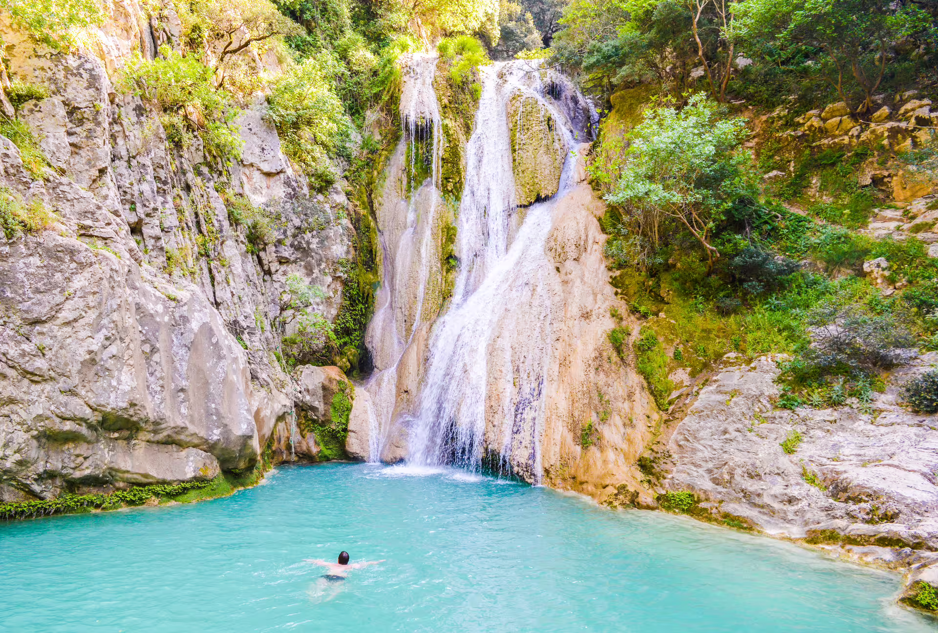 Swimmer in turquoise pool beneath Polylimnio Waterfalls on a scenic hiking tour near Kalamata, Greece